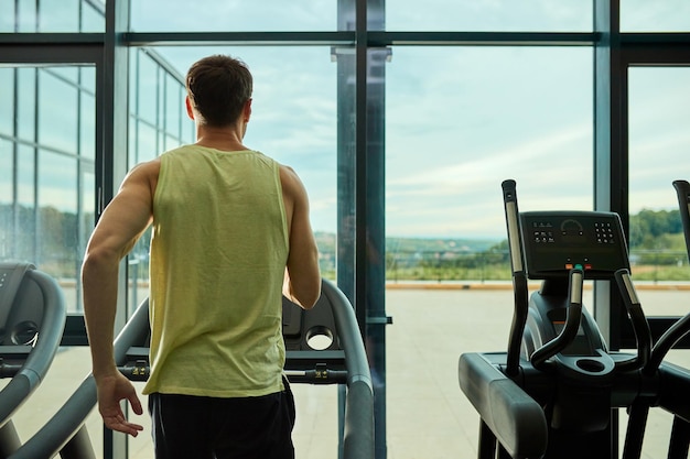 Back view of athletic man jogging on treadmill while exercising in health club Copy space