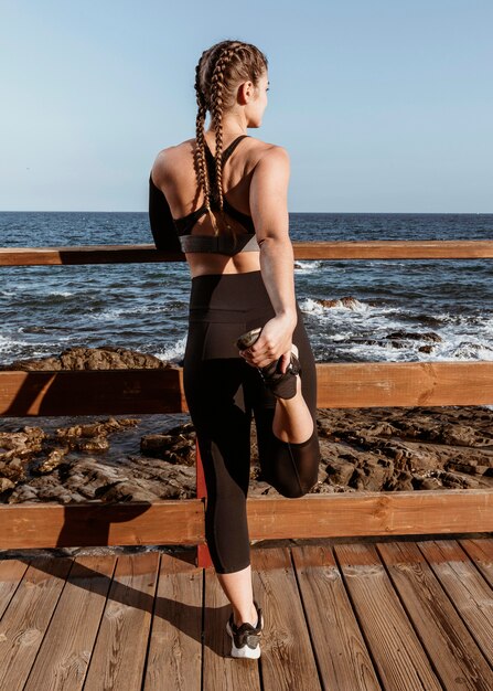 Вид сзади спортивной женщины, растягивающейся на пляже