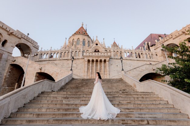 Back view of an attractive bride on the stairs of a historical building on the beautiful warm summer evening