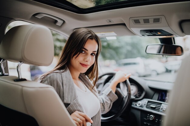 車を運転しながら彼女の肩越しに見ている魅力的な若いビジネス女性の背面図