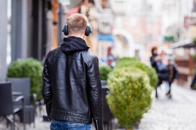 Back view blonde young man listening to music on headphones