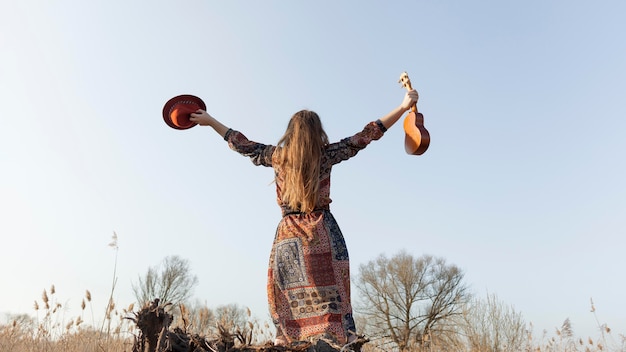 Back view of bohemian woman holding had and ukulele