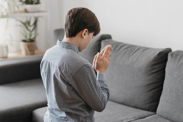 Ragazzo di vista posteriore che prega nel soggiorno