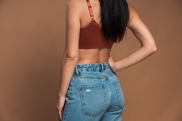 Back view of the brunette long haired woman wearing top and jeans posing at the studio over the brown wall. perfect figure concept