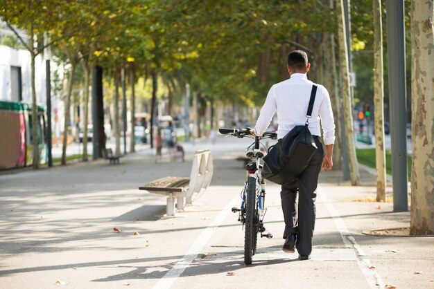 Back View of Businessman Walking with Bike in Park