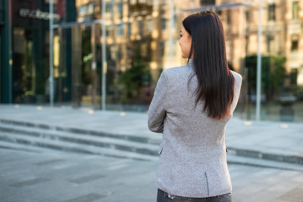 Foto gratuita vista posteriore della donna di affari che propone all'aperto con le braccia incrociate