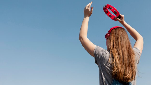 Back view of of carefree woman with headphones holding tambourine