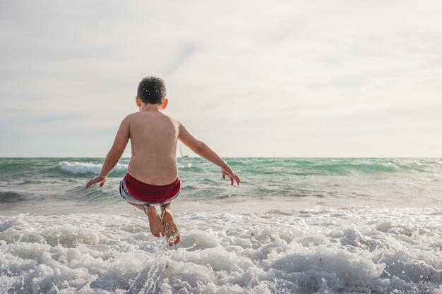 Back view of a caucasian boy jumping on the eaves of the sea