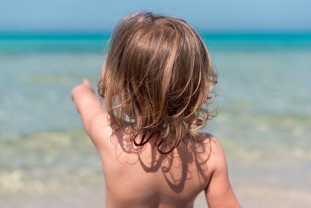 Back view of child at the beach pointing at water