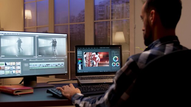夜間にホームオフィスで作業しているコンテンツ作成者の背面図。ホームオフィスのビデオエディタ。