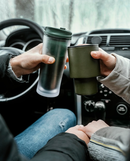 Foto gratuita vista posteriore della coppia in macchina durante un viaggio brindando con bevande calde