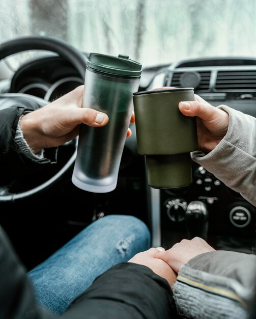 Back view of couple in the car while on a road trip toasting with warm drinks