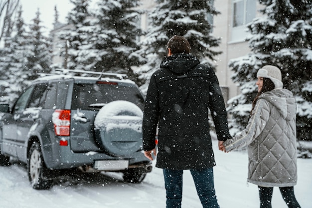 Back view of couple enjoying the snow while on a road trip with car