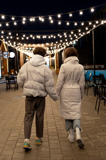 Back view of couple holding hands outdoors in lights