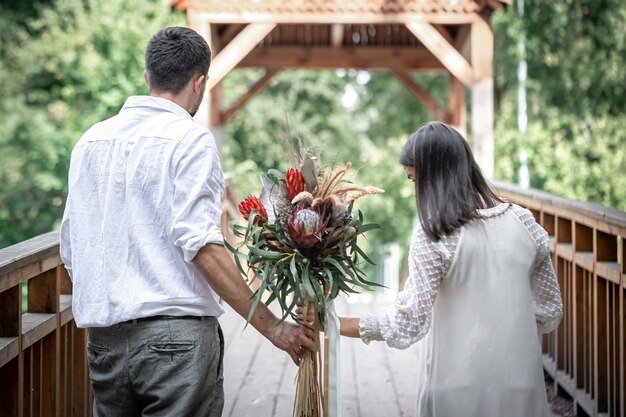 Back view, a couple in love holding a bouquet with exotic protea flowers.