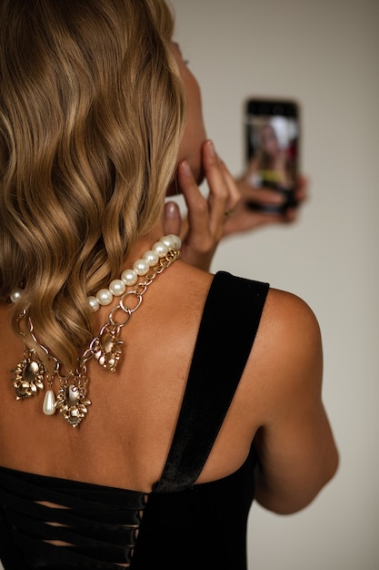 Free photo back view crop stock photo of anonymous fair-haired lady in black top and necklaces on her back taking self-portrait