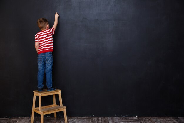 Back view of cute little kid boy writing with chalk