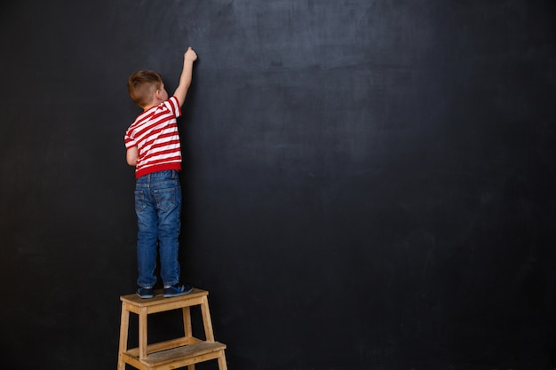 Back view of cute little kid boy writing with chalk