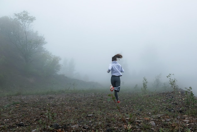 Back view of determined runner running through nature on misty weather Copy space