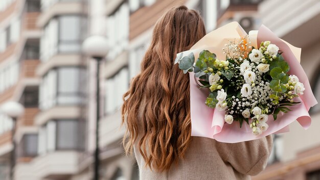 Back view of elegant woman holding bouquet of flowers outdoors