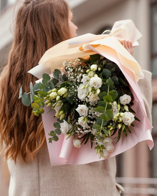 Back view of elegant woman holding bouquet of flowers outside