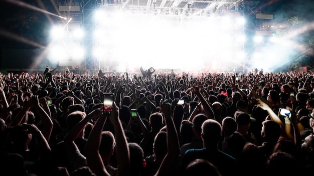 Back view of excited audience with arms raised cheering in front of the stage at music concert Copy space