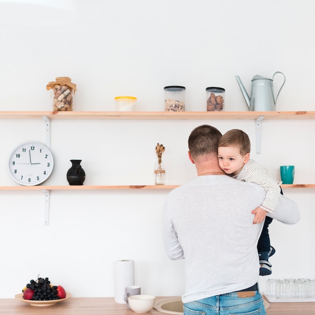 Back view of father holding child in the kitchen