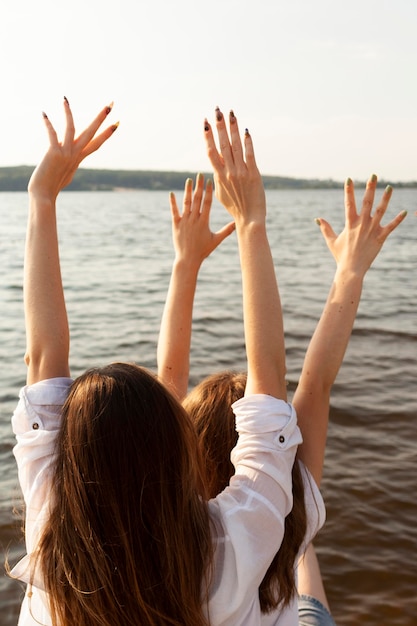 Back view of female friends at the lake with arms up