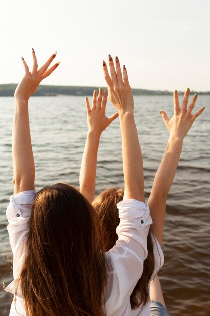 Back view of female friends at the lake with arms up