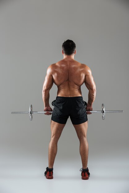 Back view full length of a muscular shirtless male bodybuilder