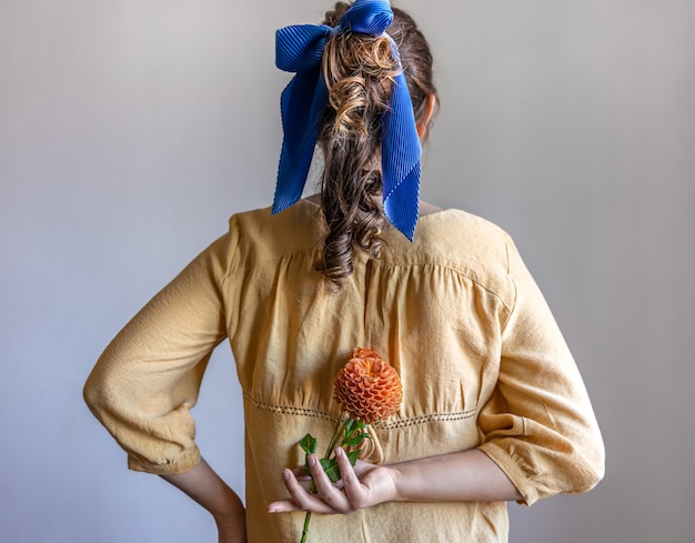 Вид сзади девушка держит цветок хризантемы за спиной на сером фоне