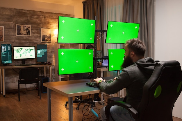 녹색 모의가 있는 여러 화면이 있는 컴퓨터 앞에 있는 해커의 뒷모습.
