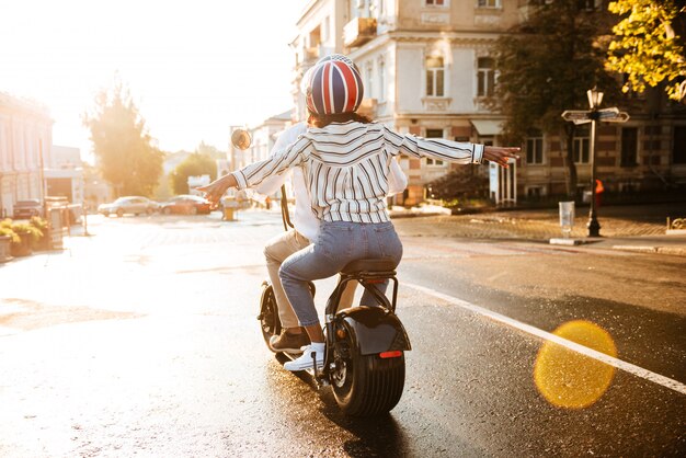 Back view of happy african couple rides on modern motorbike on the street