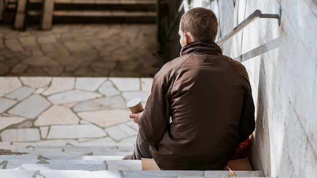 Free photo back view of homeless man with cup on stairs