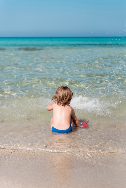 Back view of kid sitting at the shore