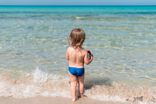 Вид сзади ребенка, идущего к воде на пляже