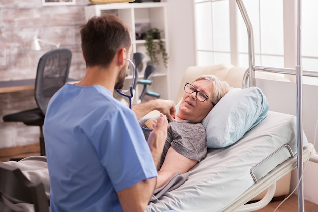 Vista posteriore del medico maschio che utilizza lo stetoscopio per controllare il cuore della donna nella casa di cura.