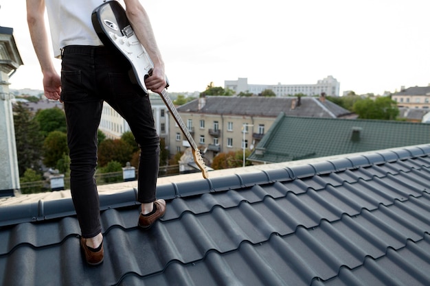 Back view of male musician on roof top holding electric guitar