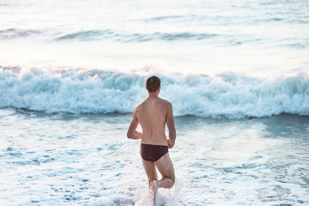 Back view of male swimmer getting in the ocean