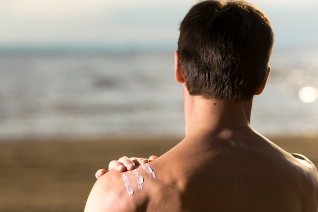 Free photo back view man applying sunscreen lotion