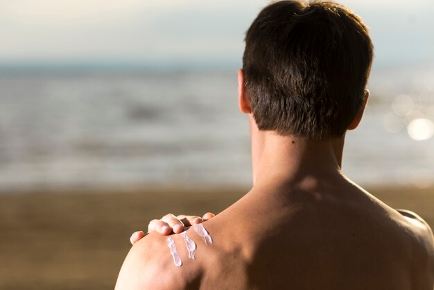 Free Photo back view man applying sunscreen lotion