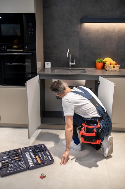 Back view of man crouching near kitchen sink