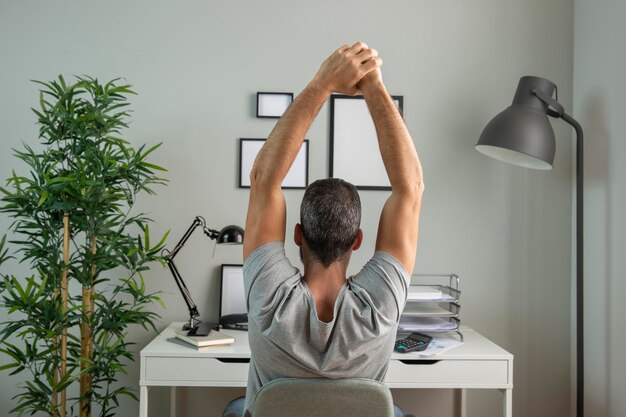 Back view of man at desk stretching while working from home