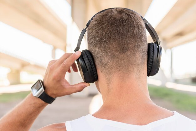 Back view man listening to music through headphones