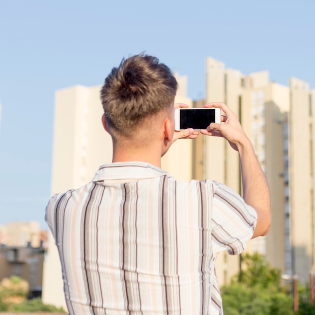 Back view of man taking pictures outdoors with smartphone