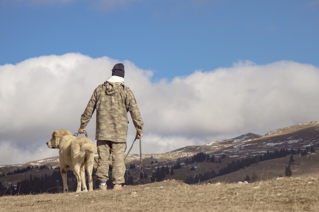 Back view of a man with his dog on a high hill enjoying the views