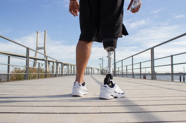 화창한 날 기계 다리를 가진 남자의 뒷모습. 검정 반바지와 흰색 운동화를 신고 훈련하는 동안 사진을 찍은 스포츠맨. 스포츠, 장애, 취미 개념