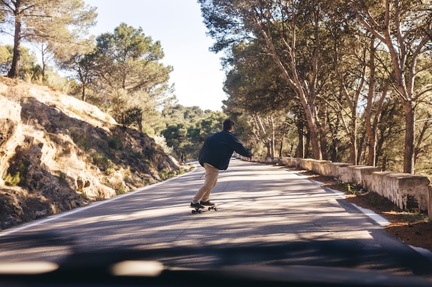 道路上のスケートボードを持つ男の背面図