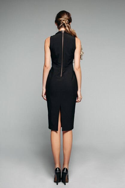 Вид сзади модели с хвостом в классическом платье без рукавов и черных высоких каблуках Изолировать на сером