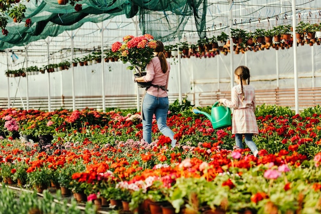 温室で働いている間花の世話をしている母と彼女の小さな娘の背面図